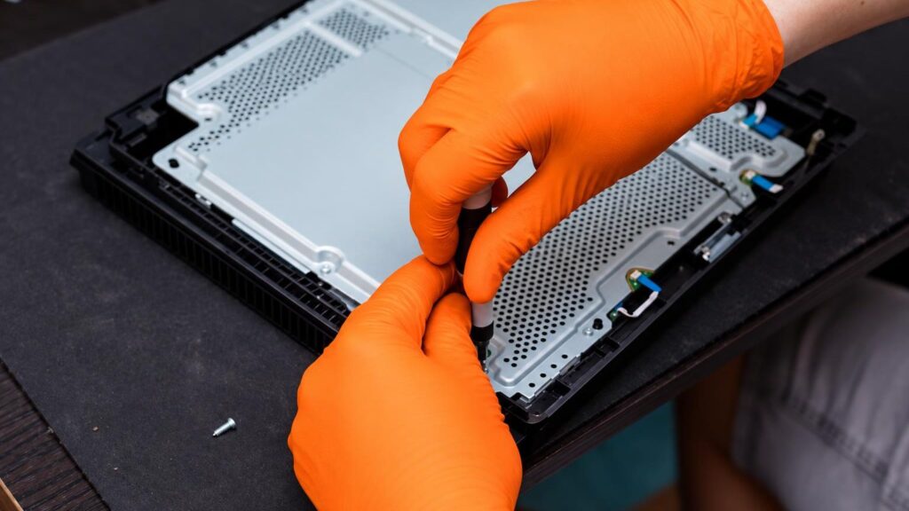 A technician repairs a game console under the light of a workbench