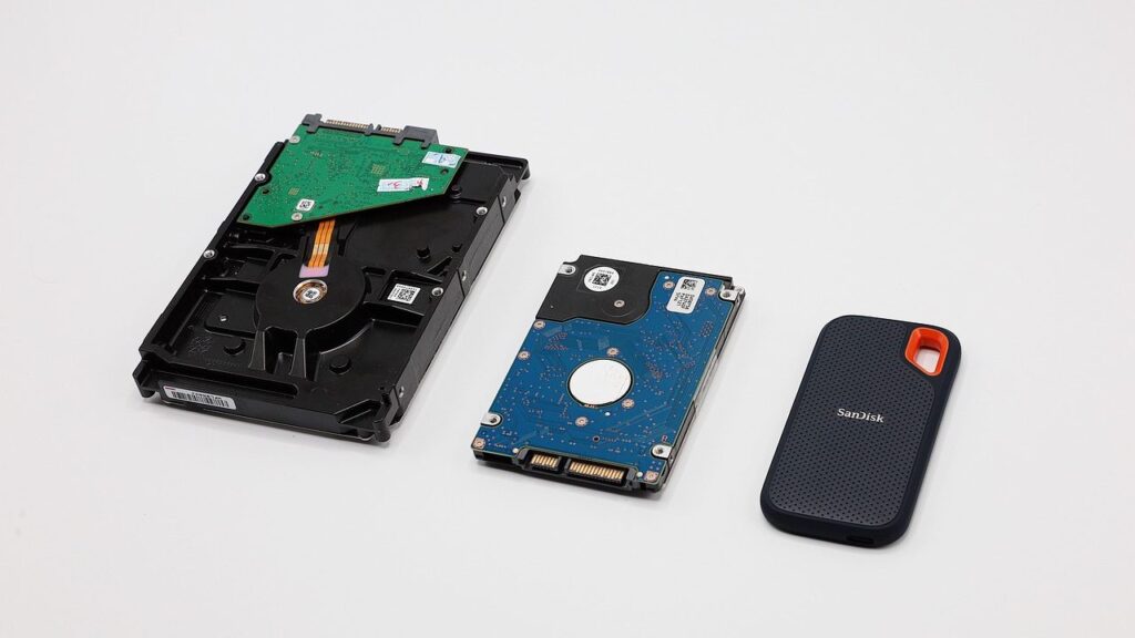 Atidarytas HDD diskas su magnetine plokštele ir skaitymo galvute šalia kompaktiško SSD